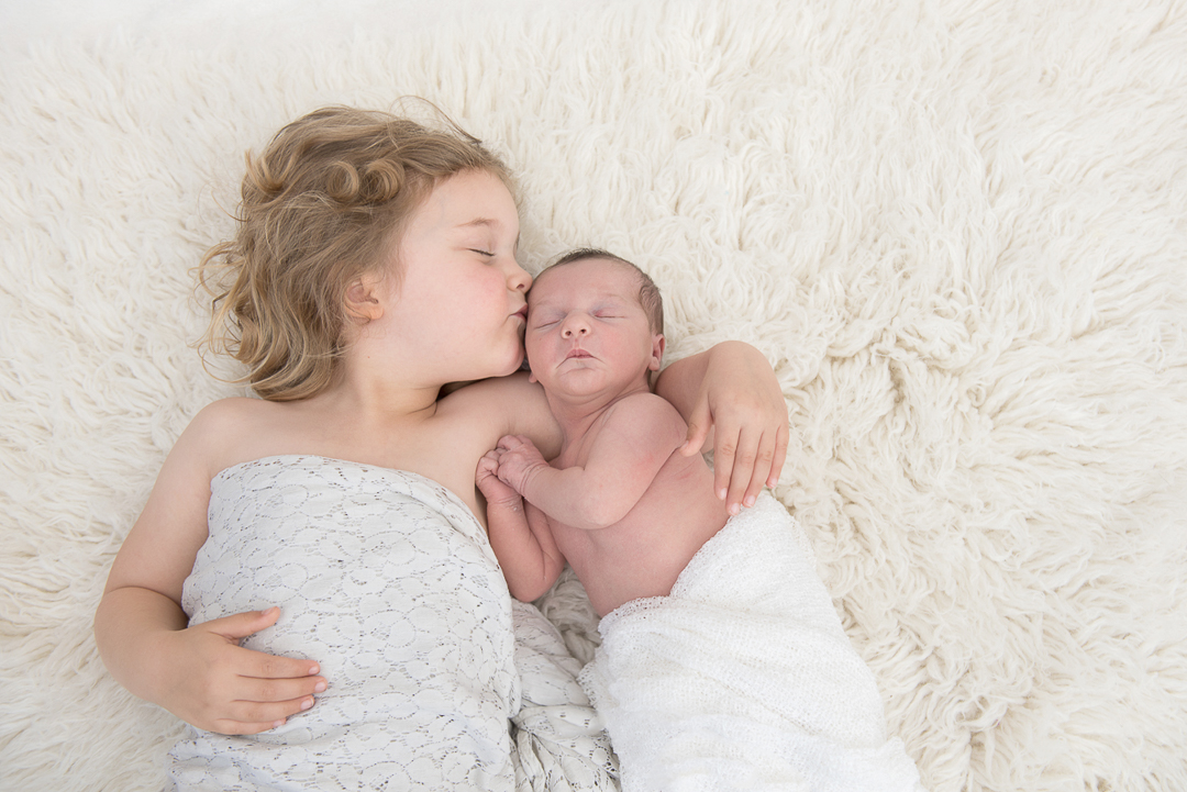 sister kissing newborn sibling during newborn session in norfolk