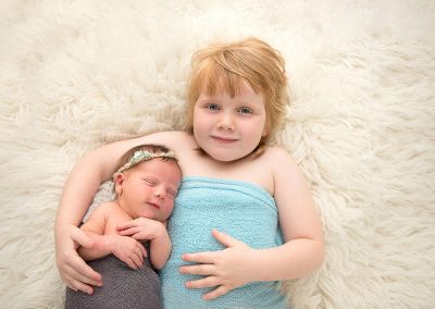newborn baby with sister on rug cuddling during newborn photography session in norfolk