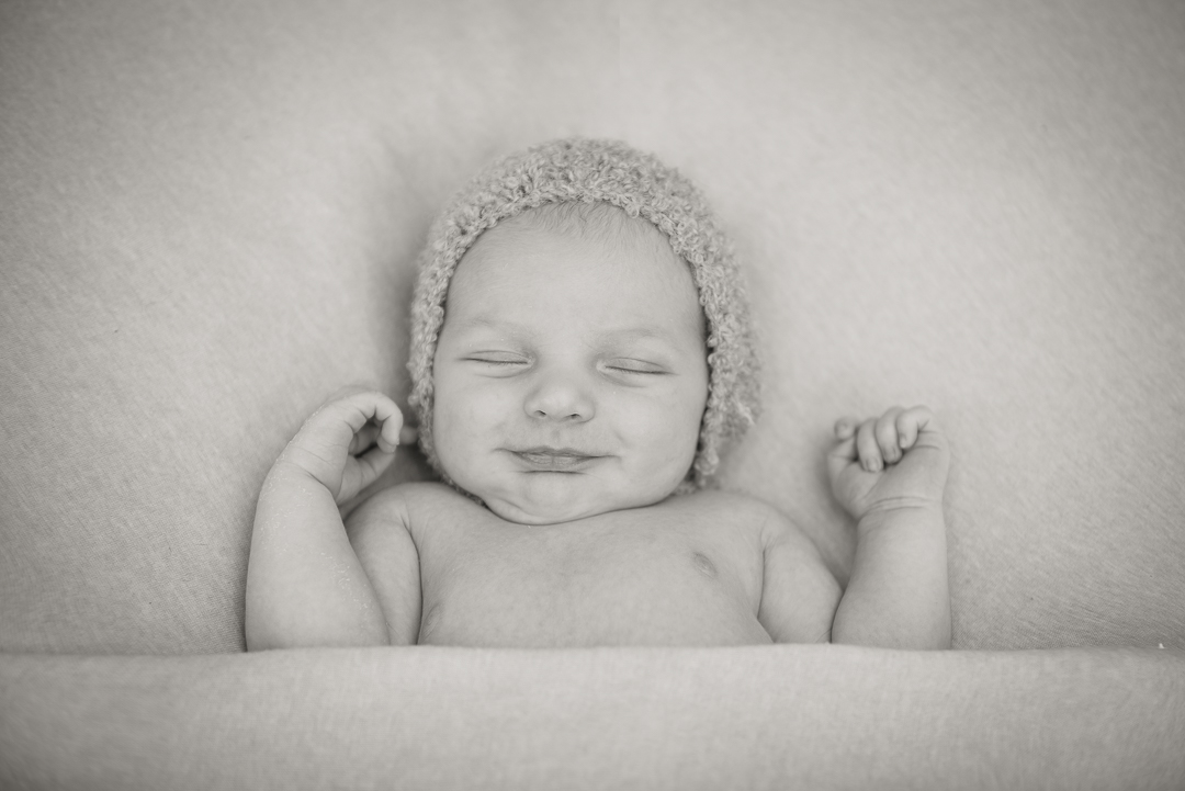 black and white photograph of baby smiling laying on back during newborn photography session
