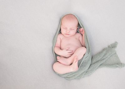 baby sleeping on back with green wrap during newborn session in norfolk