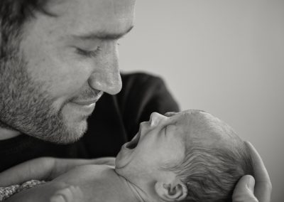 newborn baby yawning as dad smiles during at home newborn session in norfolk