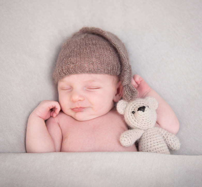 newborn baby wearing hat smiling with teddy during norfolk newborn photography session